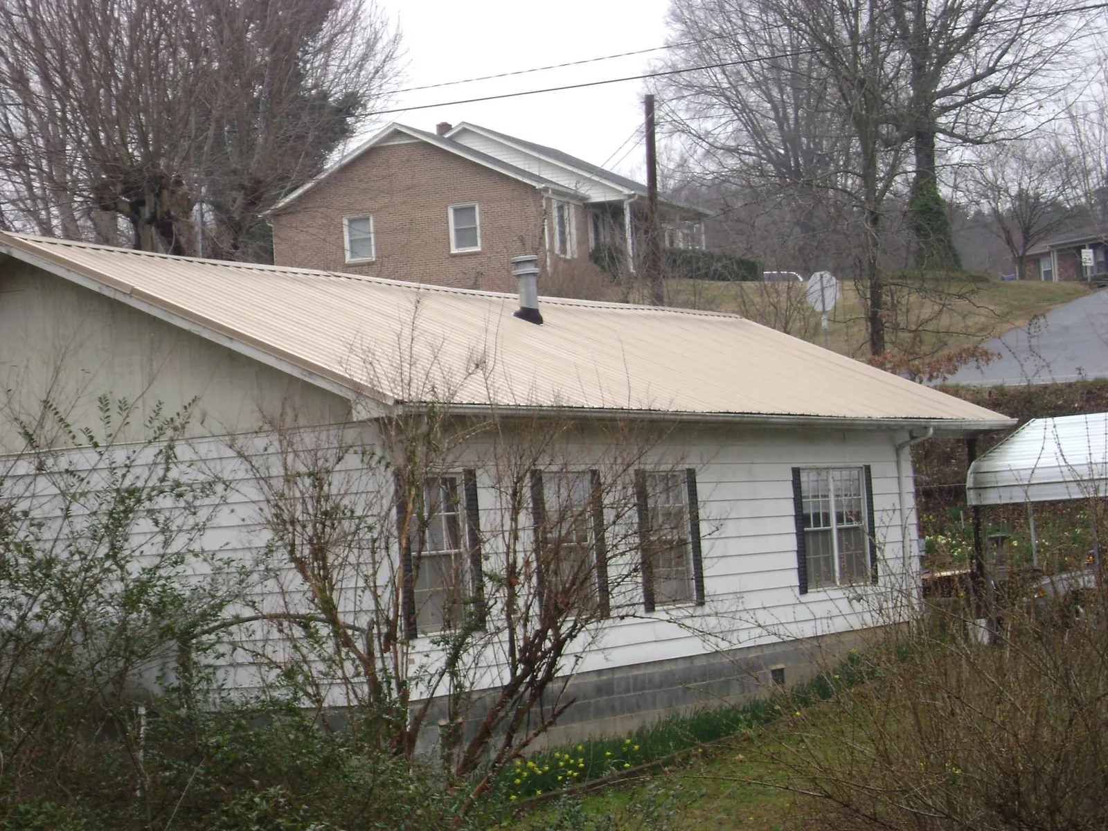 Tan metal roof on a white sided house set into a hillside — Commercial Roofing by Roofing Brothers in New Paris